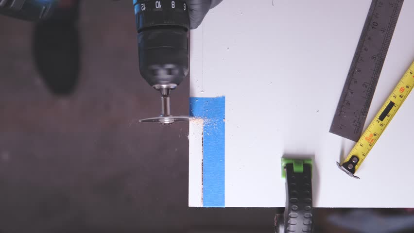 Close-up of a worker using a circular saw attachment on a drill to cut a white wooden board