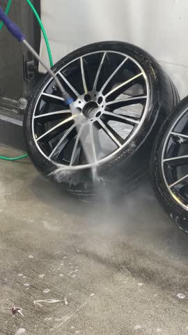 CloseUp Alloy Rim Under HighPressure Rinse, Blue Hose Sweeping Soapy Water Across Spokes, Foamy Suds Breaking Up Grime, Rapid Reveal Of Glossy Finish, Concrete Splashed, Satisfying Motion Captured
