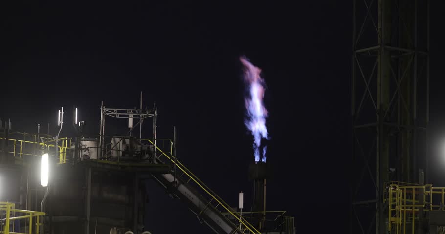 Natural gas torch nozzle at an oil refinery flame in the dark, heat haze, industrial structures, chemical plant