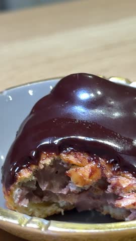 chocolate eclair with a spoon plate of chocolate covered pastries with nuts on top. The plate is white and the pastries are brown