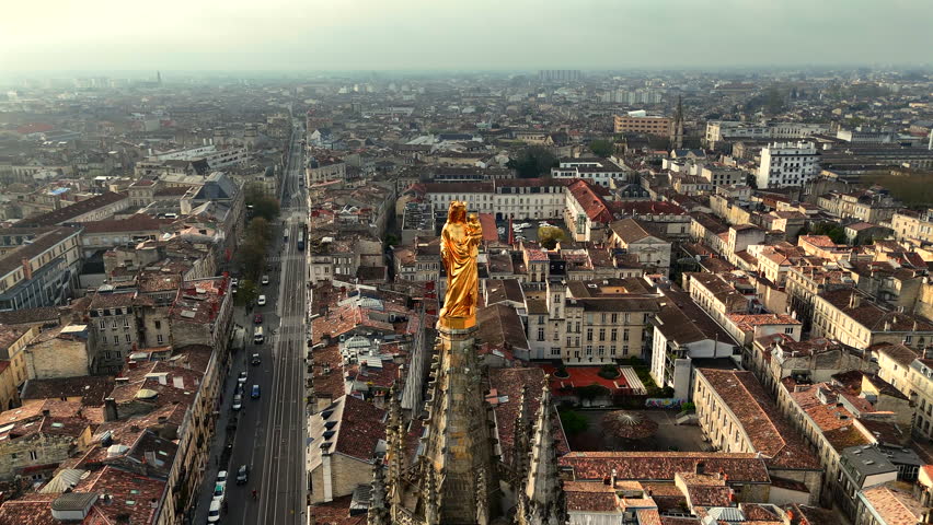 Golden Virgin Mary statue on Pey Berland Tower in Bordeaux under cloudy sky