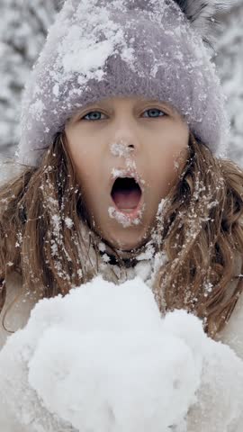 Snowy winter fun. blowing snow. Happy, cutie, pretty, little girl, dressed in warm winter clothes, is blowing snow from hands at camera, outdoors, in snowy park or forest.