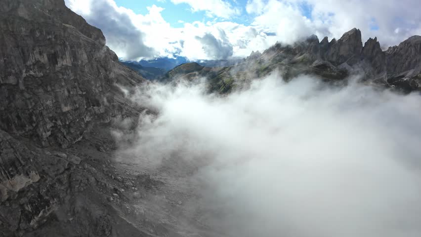 dolomites craggy summit and basin filling with thick cloud. cinematic drone frames jagged rock faces, textured scree slopes and distant sunlit ridges, creating moody high-altitude scene