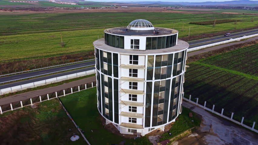 A striking round structure with large windows sits quietly in expansive greenery, reflecting the golden hues of the setting sun. Nearby, a road draws travelers through this serene landscape.