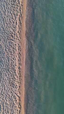 Minimalist top down split composition of turquoise sea water and beige sandy beach captured by a drone in vertical orientation suitable for travel and summer themes