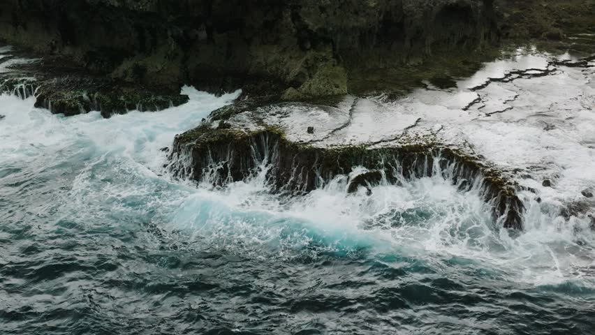 A turquoise ocean wave smashes into a rocky coast ledge creating white foam. Siargao, Philippines. Slow Motion.