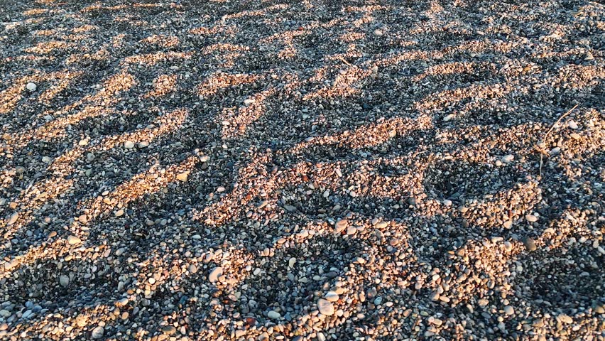 High angle close up of beach pebbles illuminated by the low angle sun creating long shadows and a rich textured ground surface pattern