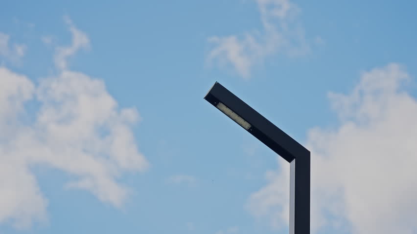 Minimalist streetlight silhouette with angular modern design against bright blue sky and clouds, showcasing urban infrastructure, geometric lines, and contemporary outdoor lighting