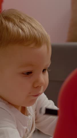 Vertical Screen: A young boy is happily drawing with a marker on a blackboard. The room is bright and colorful, creating a fun environment for creative play and learning.