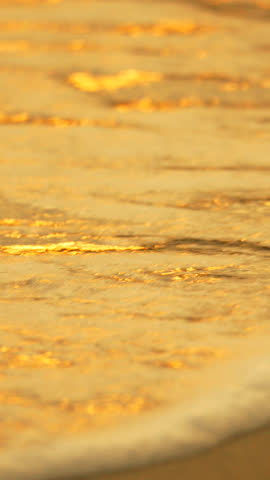 Water, waves, sand Golden sunset reflections wash over tropical beach sand in mesmerizing slow motion close up Vertical video
