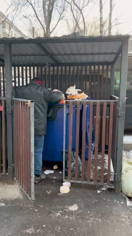 Poor old homeless man looking for food in trash cans in Moscow, Russia