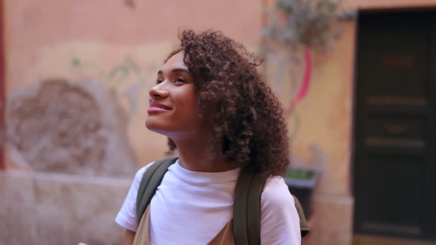 Traveler pauses in a quiet narrow alley to photograph surrounding buildings, capturing warm daylight, textured walls and the peaceful atmosphere of a charming urban environment