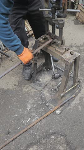 A detailed close-up shot of a factory worker manually cutting external threads on a metal pipe using a specialized threading tool. Focus on precision, industrial craft, and metal fabrication.
​