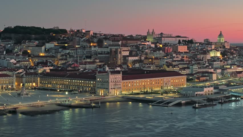 Morning lights illuminate the city of Lisbon along the river, Portugal. Aerial shot of Lisbon city center at sunrise