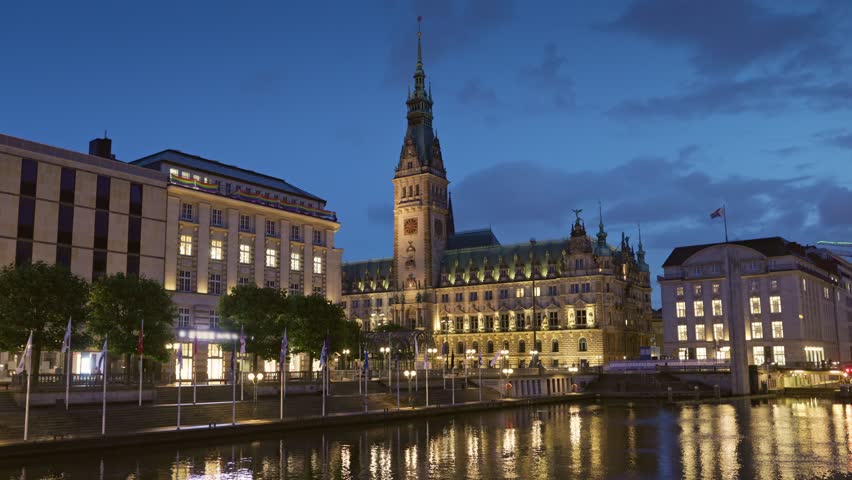 Evening pannin view of Hamburg City Hall at night with lights reflecting on the water beside the building. Humburg, Germany after sunset