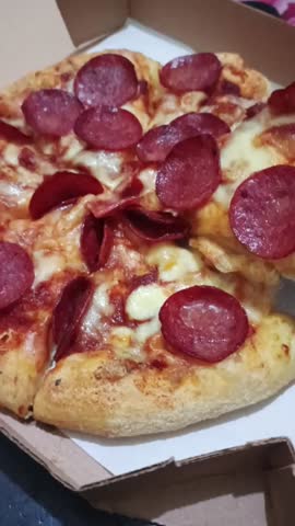 A hand taking a slize of cheesy pepperoni pizza from a pizza box