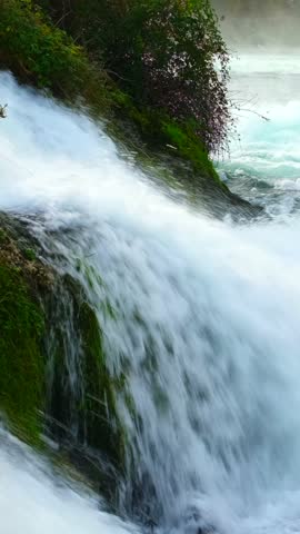 Water flows over rocks in a natural setting near a river in the afternoon light