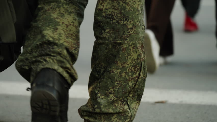 Close-up view of soldiers in camouflage uniforms marching along a city street, sturdy combat boots striking the pavement in steady steps during a patrol or training formation