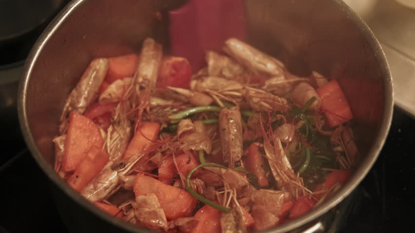 Cooking seafood. Shrimp shells. Chef hand stirring fried ingredients for bisque soup. Tom yum kung with carrots green herbs spices in hot steaming pot.