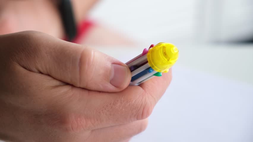 The person holds in hand a multi-colored ballpoint pen, the nibs of which slide out and retract with clicks. Close-up of various colors of office and school stationery. High-quality 4k footage.