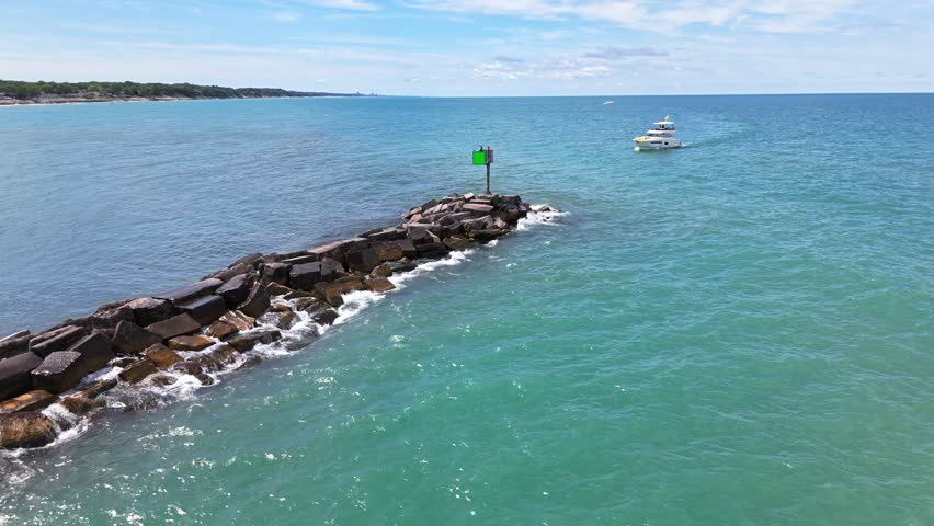 Low aerial orbit of jetty at New Buffalo Beach, Michigan, with a boat cruising in on a beautiful summer day on Lake Michigan
