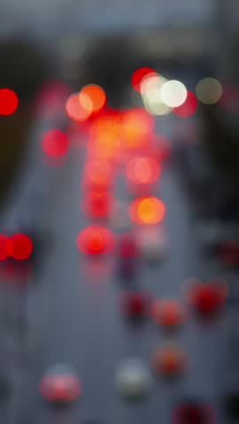 Defocused evening city traffic with red taillights and white headlights moving along a rain-soaked road, forming bokeh patterns and reflections during the rushhour commute