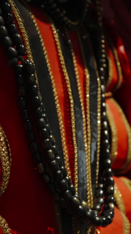Close-up of ornate traditional costume with layered black bead necklaces, gold-trimmed embroidery, and vibrant red fabric, capturing texture, shimmer, and ceremonial elegance