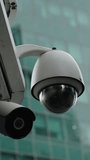 Close-up of an outdoor PTZ dome security camera on a metal arm beside a bullet camera, set against a modern glass office facade, highlighting urban surveillance and monitoring. - Powered by Shutterstock - Get 15% off with code: PIKWIZARD15