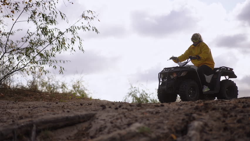Slow motion. Female rider on quad sandy trail wearing yellow jacket navigating rough slope low angle wheel shots dusty forest backdrop closeup tire action