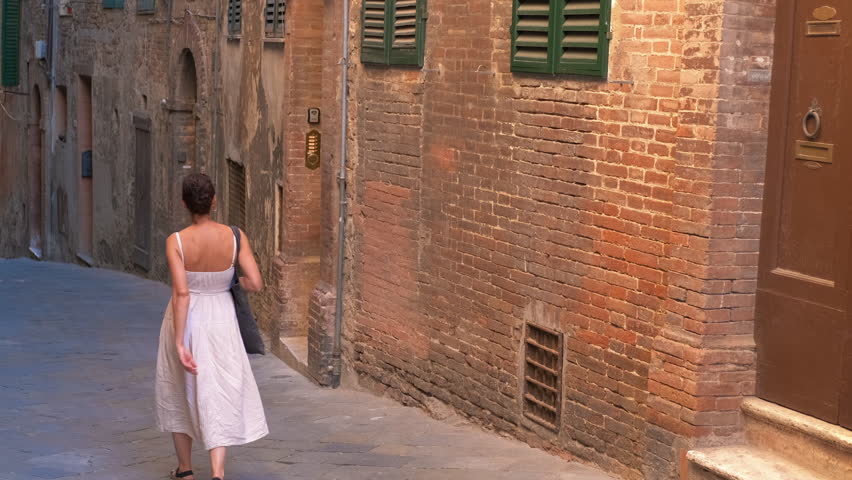 Woman walking down a narrow street in a picturesque italian town. Tourist walking alone down a narrow street in an old italian town with brick walls and green shutters, enjoying the atmosphere