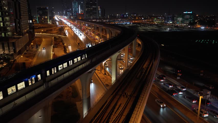 Drone video of Riyadh Metro moving out of KAFD metro station at night showing the roads and the cityscape in Riyadh, Saudi Arabia