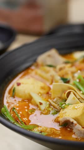 Macro view of bubbling spicy hotpot soup as spoon lifts tofu, meat, and noodles