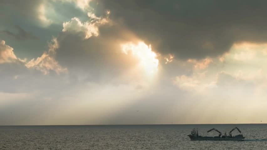 Fishing boat sailing on the ocean under dramatic sunbeams