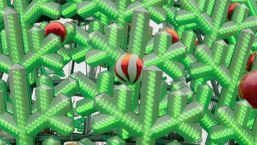 Close-up of a large LED Christmas tree installation with glowing green lights and red ornaments, creating a vibrant festive holiday atmosphere.