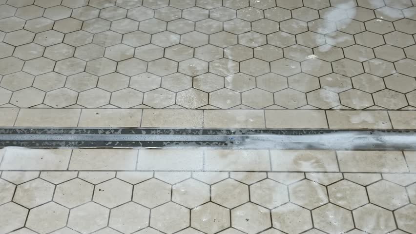 A Wet Hexagon-Tiled Floor is Being Cleaned, with Soap Suds Visible Near a Yellow Bucket - Tilt Shot