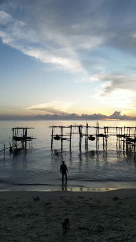 Aerial top view of colorful local fishing boat docked at the sandy beach with ocean wave crashing on the shore.
