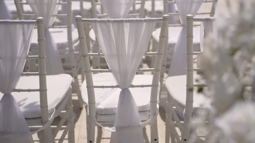 Rows of white chairs are set up for a wedding ceremony in an outdoor venue. Soft fabric drapes add a special touch for the guests attending this joyful celebration.