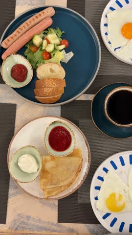 Breakfast spread with fried eggs, coffee, bread, sausages, pancakes, and sauces on a table video