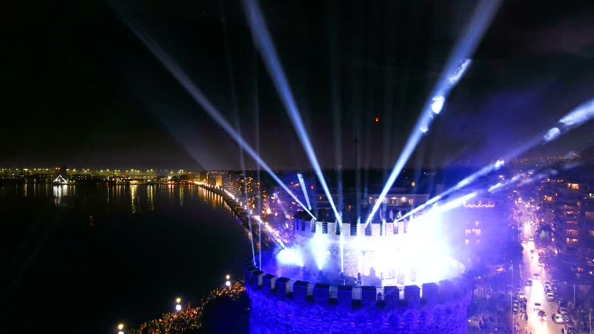 Thessaloniki, Greece, 31 Dec 2024: The White Tower glows with vibrant lights as beams radiate into the night sky, marking the city’s New Year transition.