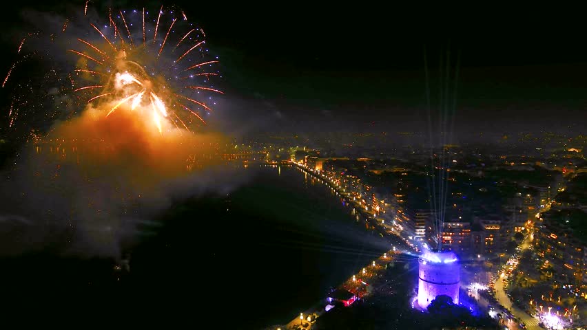 Thessaloniki, Greece, 31 Dec 2024: The White Tower glows with vibrant lights as beams and fireworks illuminate the night sky, marking the city’s New Year transition.