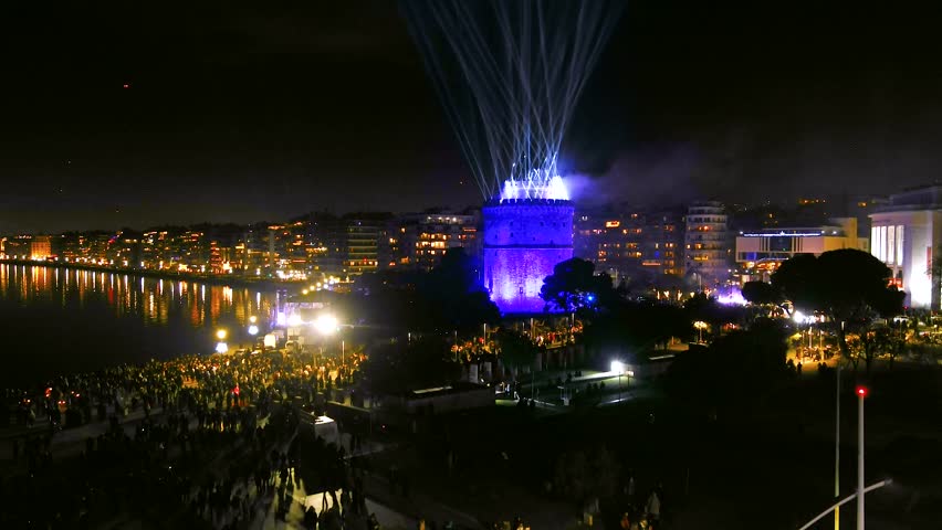 Thessaloniki, Greece, 31 Dec 2024: The White Tower glows with vibrant lights as beams and fireworks illuminate the night sky, marking the city’s New Year transition.