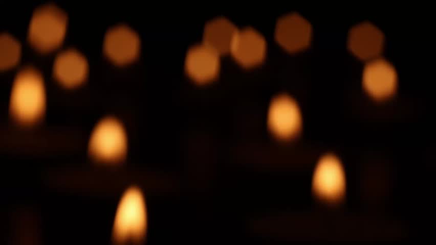 Out-of-focus candle flames flicker in warm darkness as airflow moves through the scene, causing the glowing shapes to weaken and gradually extinguish while soft light fades into black