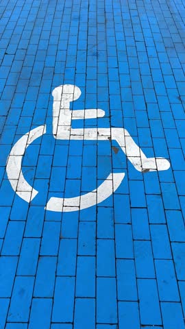 Close-up of the universal accessibility symbol painted on a vibrant blue brick pavement, symbolizing inclusivity and accessibility for people with mobility impairments. This visually clear marking ens