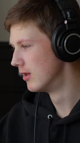 Vertical close-up of a musician singing with headphones on in a home studio.