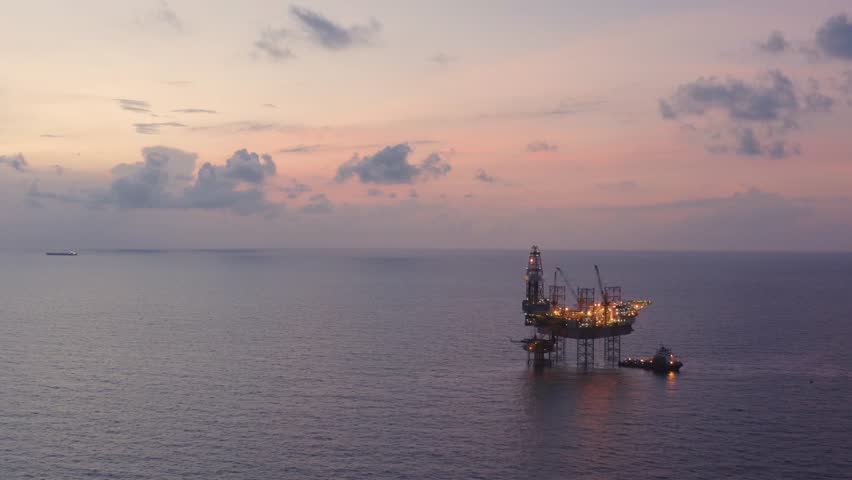 Aerial view from a drone of big jack up offshore drilling oil rig, production platform and supply vessel In the ocean during sunset - Oil and Gas Industry
