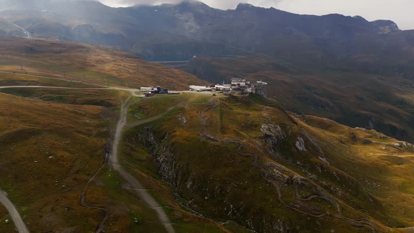 Push in aerial establishing shot of a hotel surrounded by a green field in Cervinia, Italy, Aosta Valley, Valle d’Aosta, showing alpine scenery