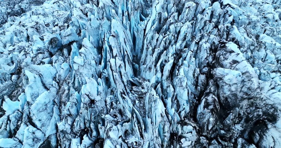 A dramatic establishing aerial shot revealing deep ice fractures and sharp ridges carved into a rugged glacier surface, showcasing powerful natural structure and frozen geological texture.