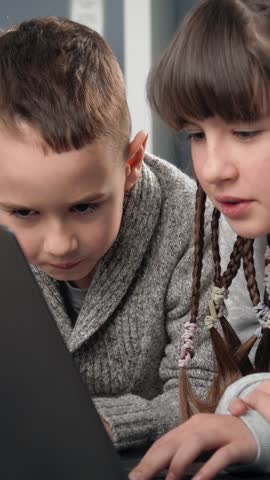 Two children focus on a laptop while learning new skills indoors.