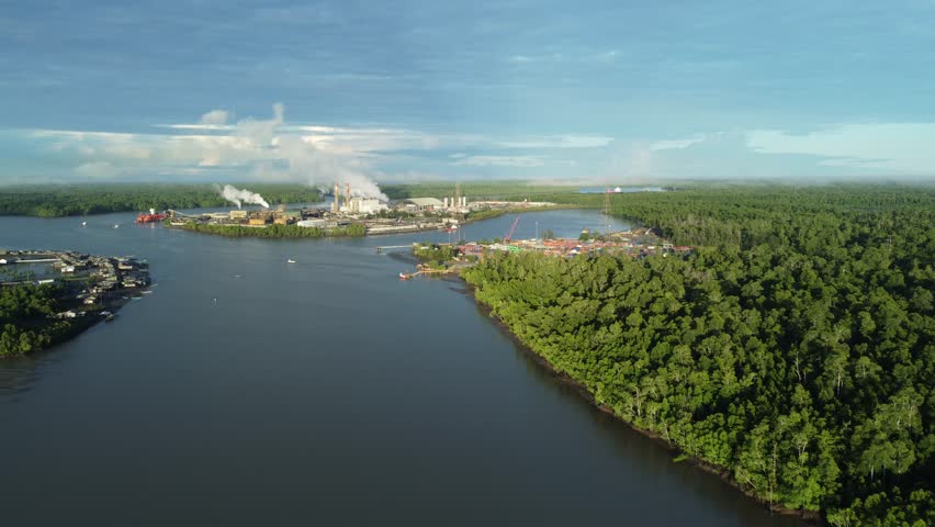 Aerial view of Karaka Island, Papua, with gold mining facilities of PT Freeport in the background, featuring industrial port, cargo ship, and river landscape.