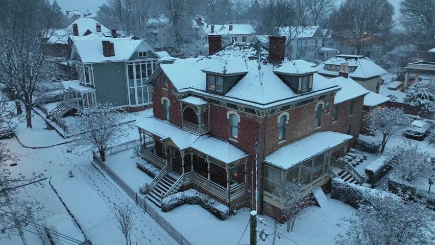 Aerial top down of Victorian brick house in America covered in fresh snow, soft blue winter light. Historic architecture and quiet neighborhood in calm seasonal atmosphere.